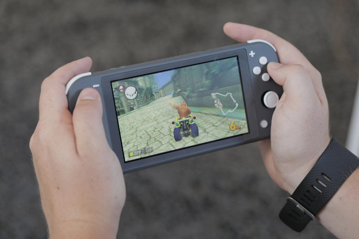 Person holding a gray Nintendo Switch Lite console while playing The Legend of Zelda, with the game displayed on the screen.