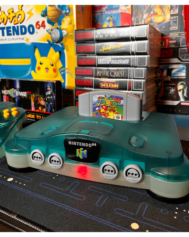 Front view of a Funtastic ice blue Nintendo 64 console with Super Mario 64 cartridge inserted and power light on.