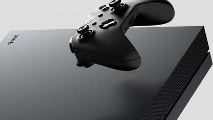 Front view of a black Xbox One X gaming console with matching black wireless controller, disc drive, and textured finish