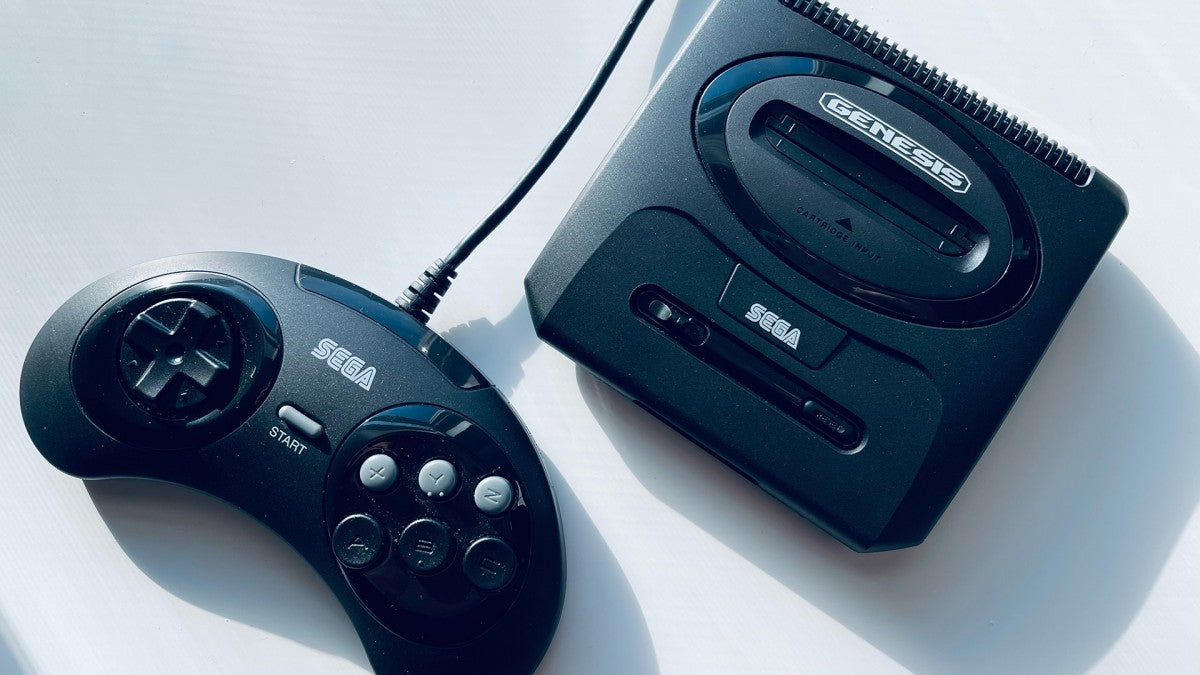 Top down view of a Sega Genesis Mini 2 console with a controller next to it, showing the console’s top surface, controller ports, power button, logo, and the full layout of the controller.