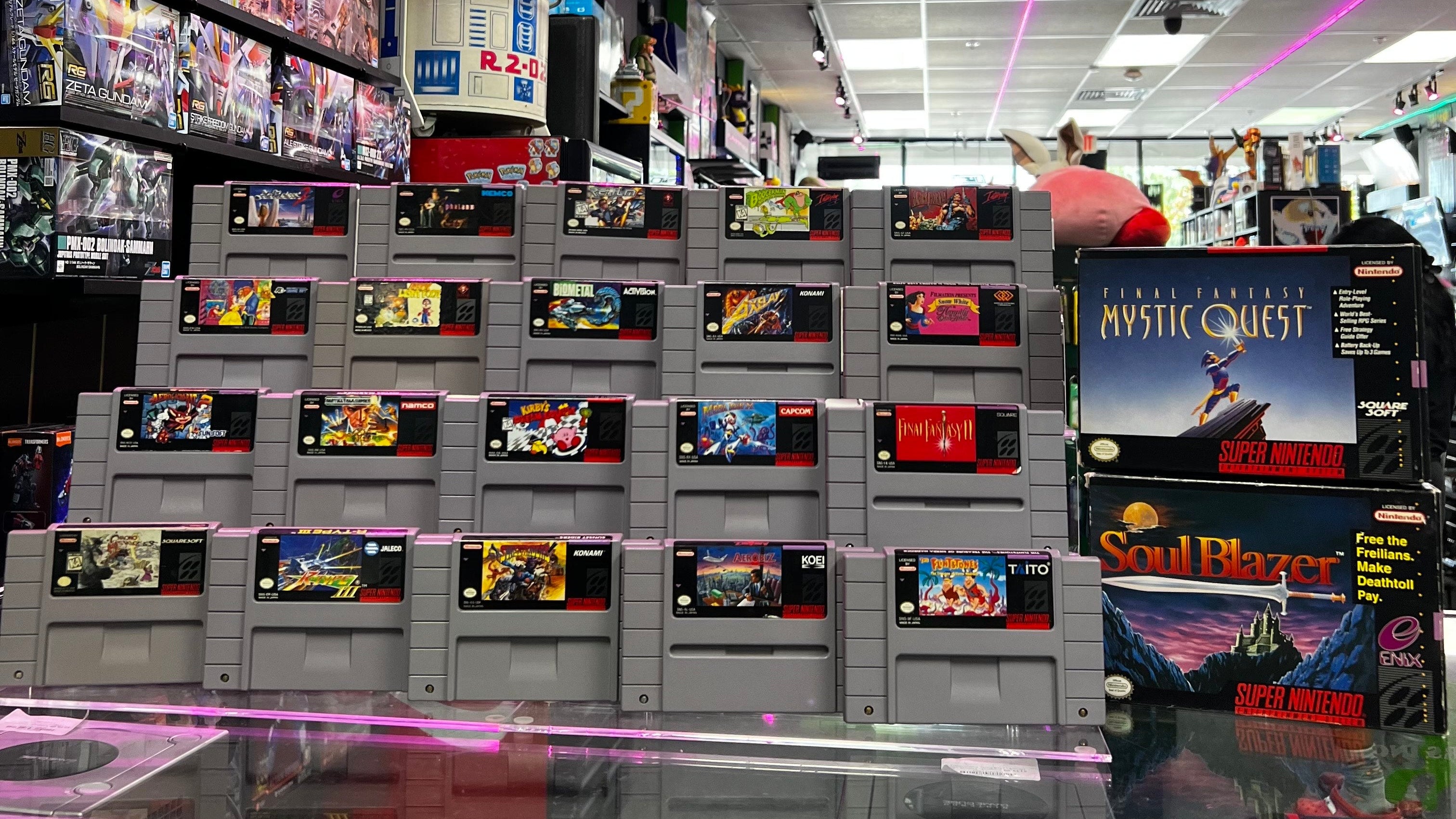 Stack of vintage SNES video game cartridges with a display case in the foreground at Gamers Inc Orlando Gamers Go Retro