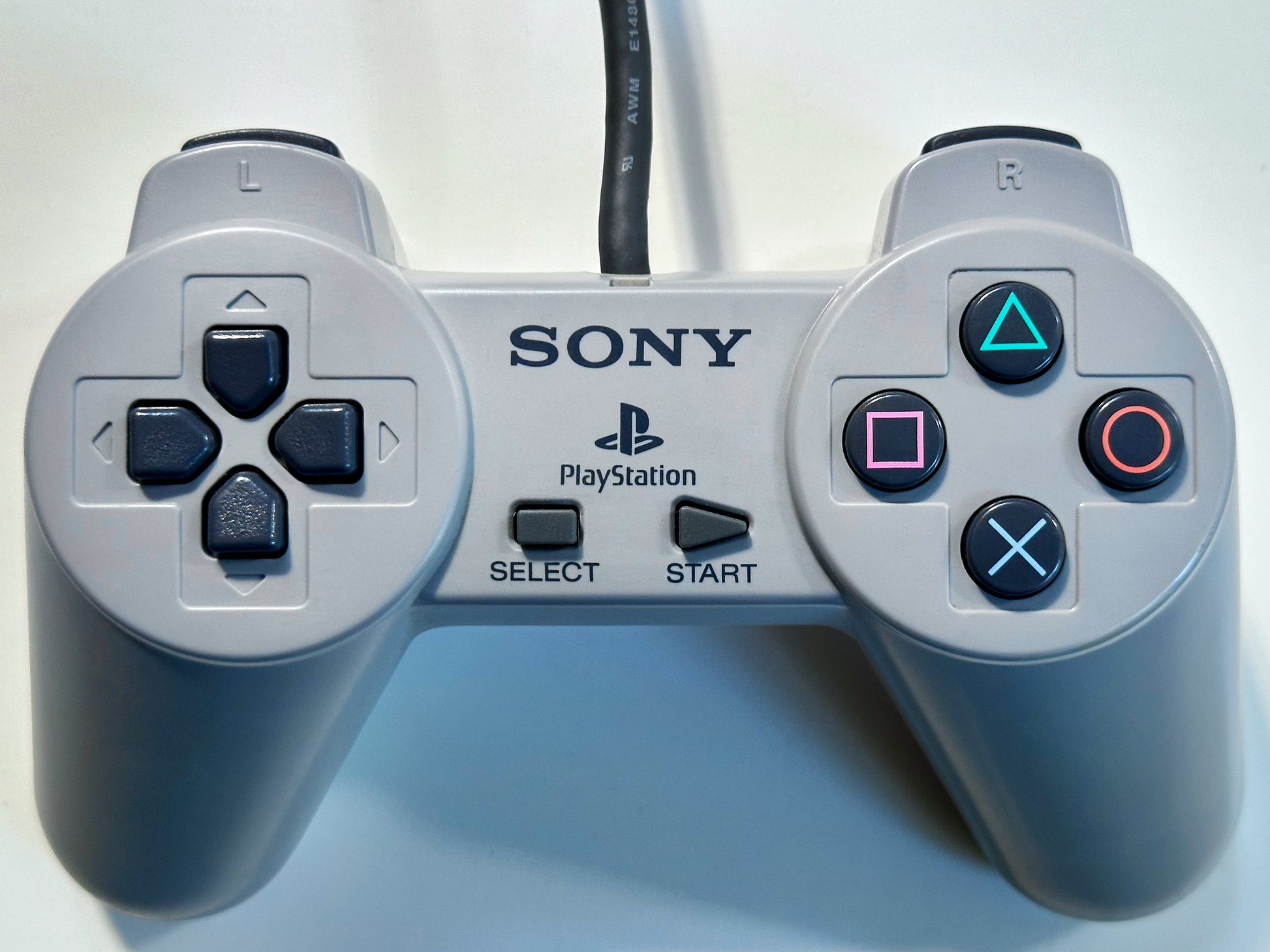 Original Sony PlayStation 1 controller with gray finish featuring directional pad, four action buttons, start and select buttons, and dual shoulder buttons