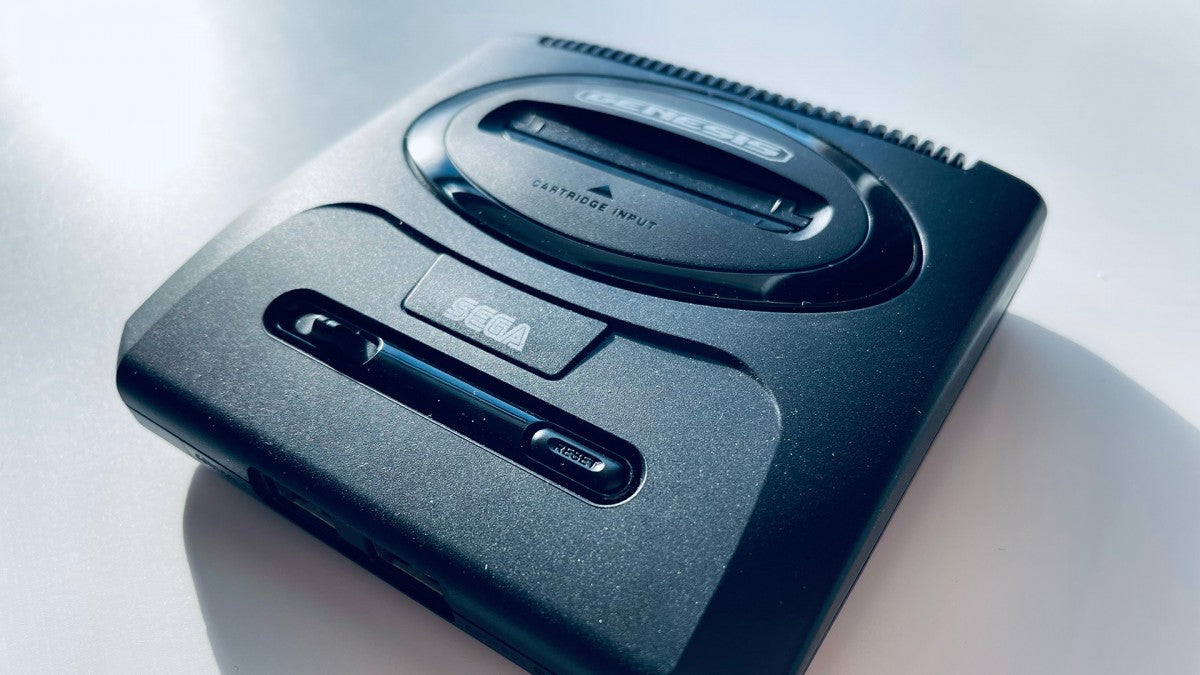 Front angled view of a Sega Genesis Mini 2 console showing the top surface, controller ports, power button, and logo from a slight side perspective.