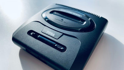 Front angled view of a Sega Genesis Mini 2 console showing the top surface, controller ports, power button, and logo from a slight side perspective.