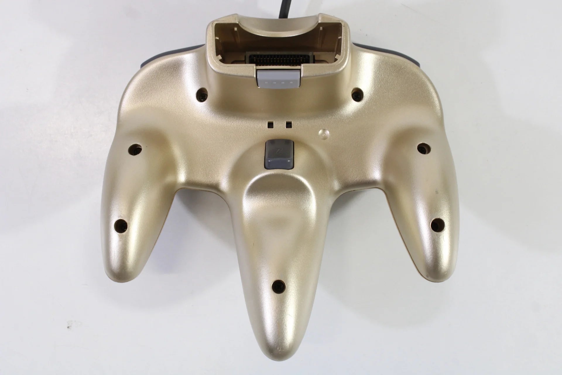 Bottom view of the gold Nintendo 64 controller, showing ergonomic contours, connector port, and structural design for stable grip during gameplay