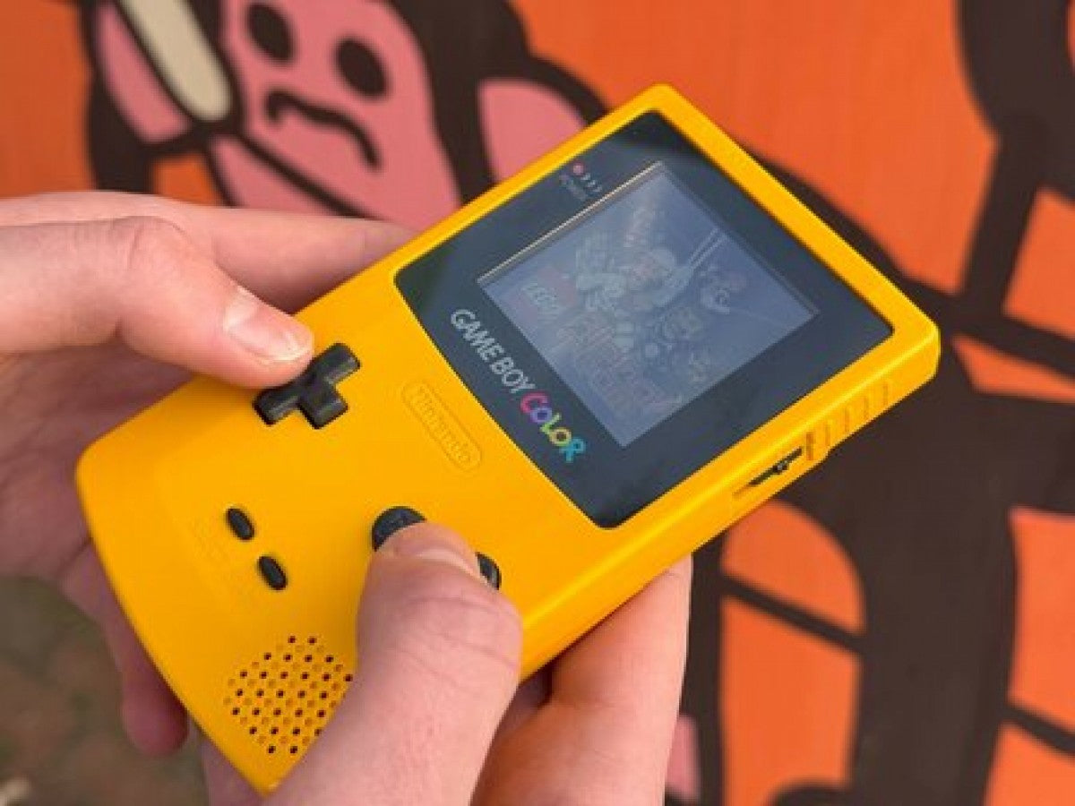 Hand holding a yellow Nintendo Game Boy Color while pressing buttons and playing a game.